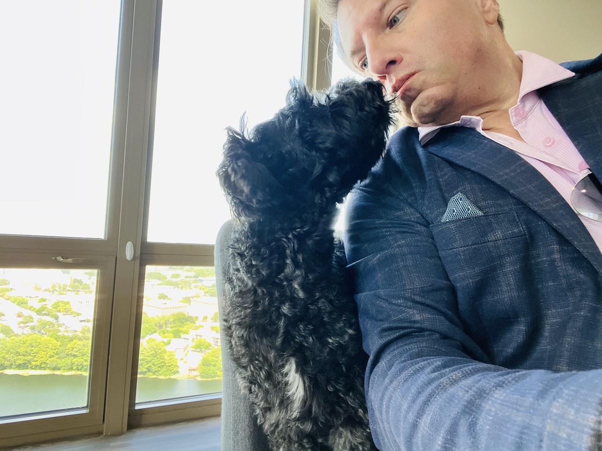 Brian Calfano nose-to-nose with his dog, Mr. R&ecirc;ve, by a window overlooking the city