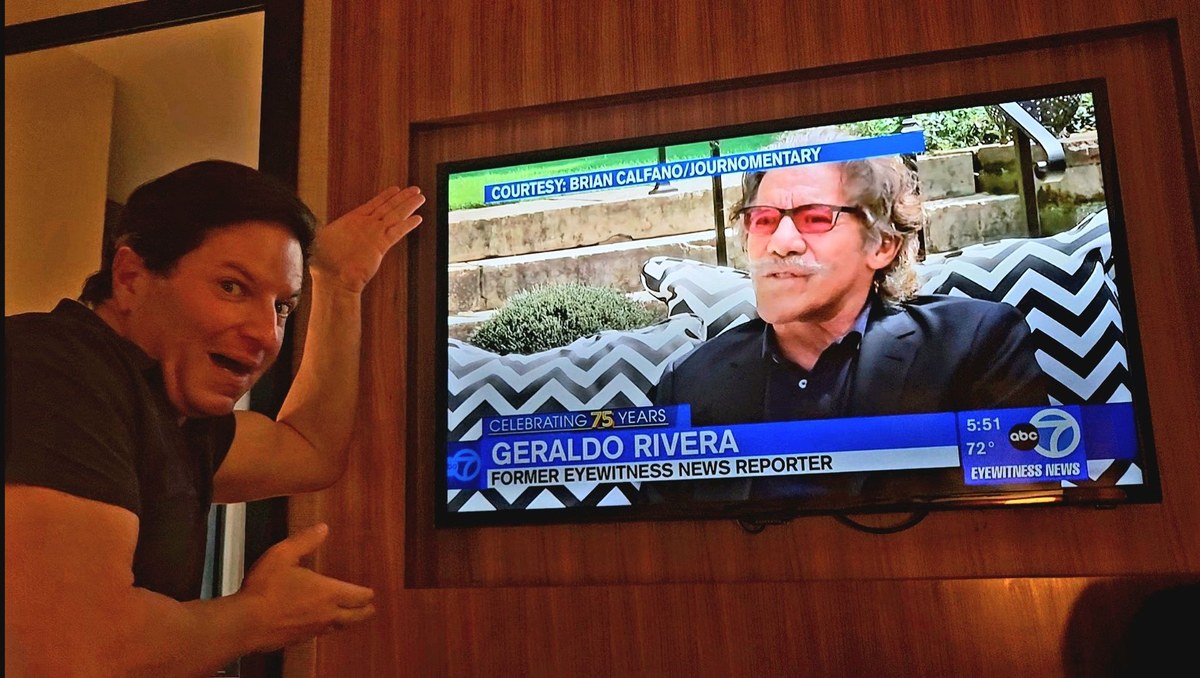 Brian Calfano pointing at a TV screen showing WABC-TV's 75th anniversary special featuring Geraldo Rivera, with an on-screen credit reading Courtesy: Brian Calfano/Journomentary