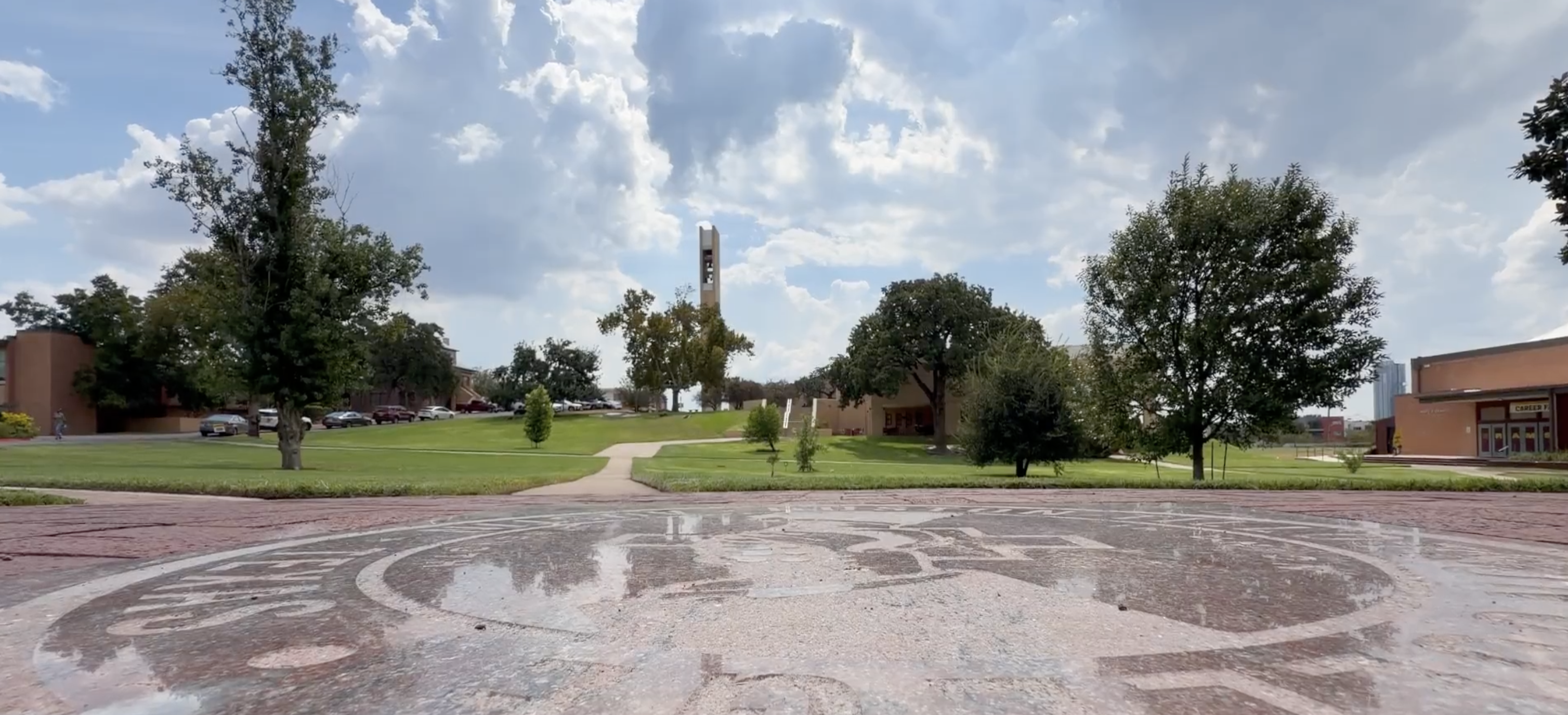 The Huston-Tillotson University campus quad in Austin, with the clock tower in the distance under a cloudy sky.