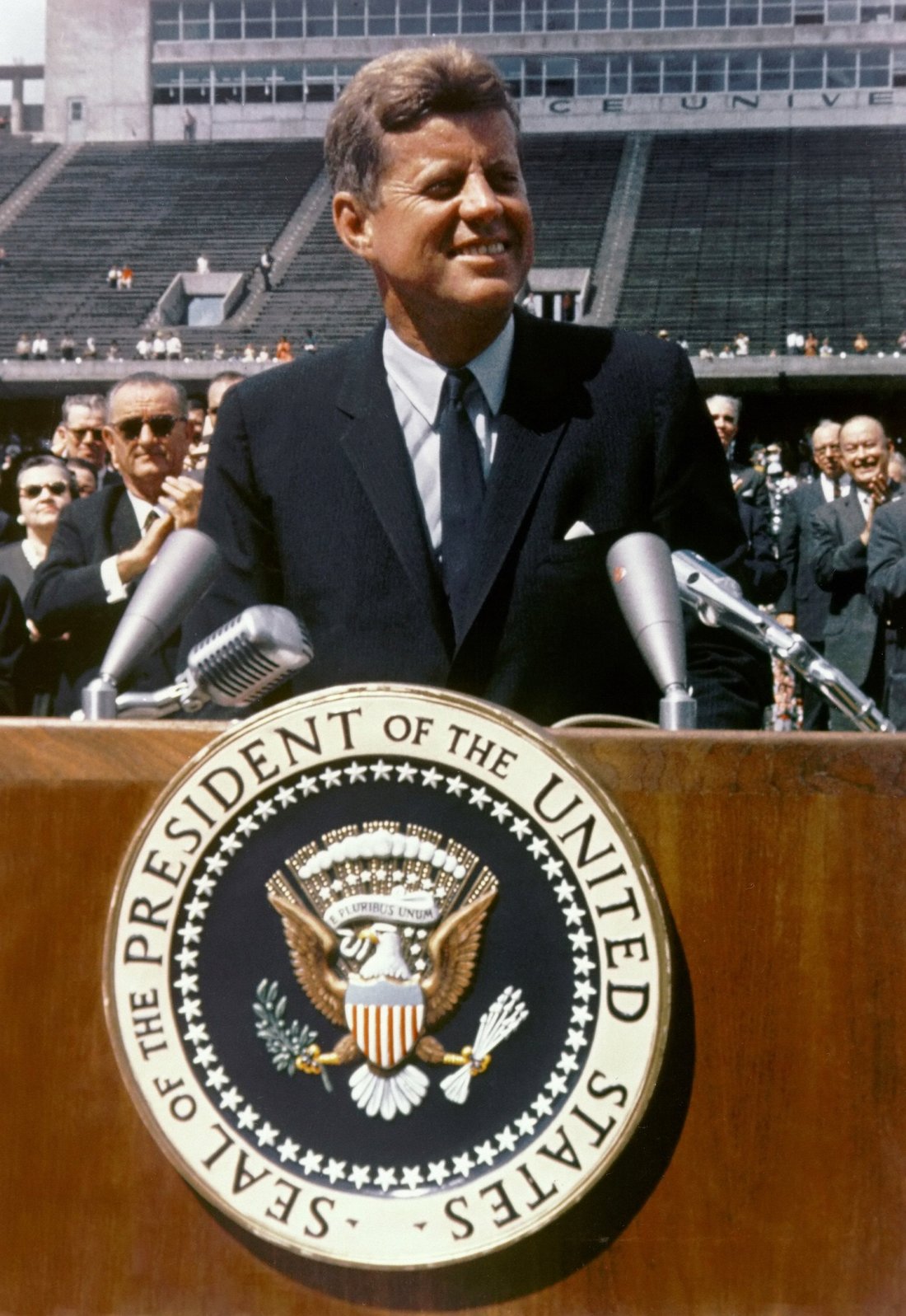 President John F. Kennedy smiling at the podium bearing the Presidential Seal during his "We choose to go to the Moon" address at Rice University, September 12, 1962.